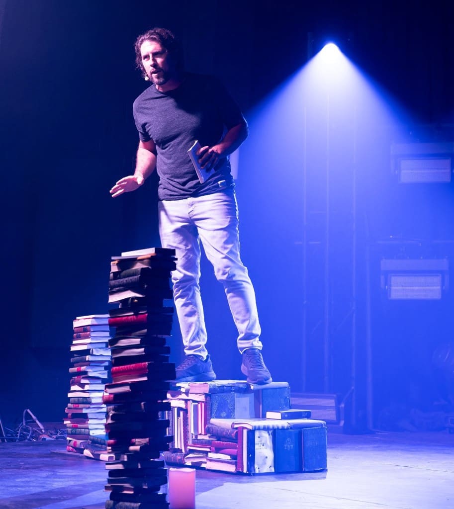 Artiste sur une scène éclairée, debout sur des piles de livres