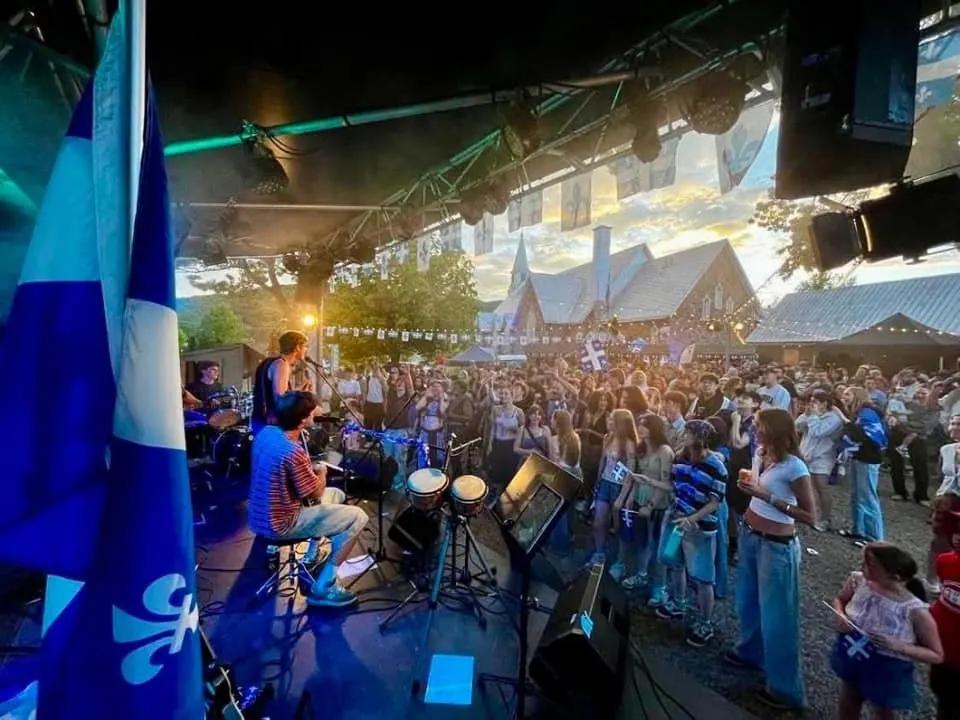 Concert en plein air à la Scène Éclat audiovisuel - Espace festif : foule et drapeaux du Québec devant l'église de pierre au coucher du soleil